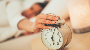 A hand hitting the snooze button on an alarm clock, a habit that disrupts sleep cycles and increases morning brain fog.