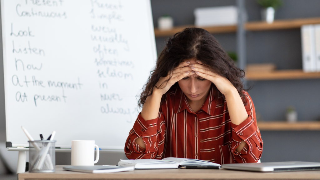 A frustrated woman sitting at a desk with her head in her hands, illustrating the feeling of "brain fog," low energy, and fatigue from poor nutrition.